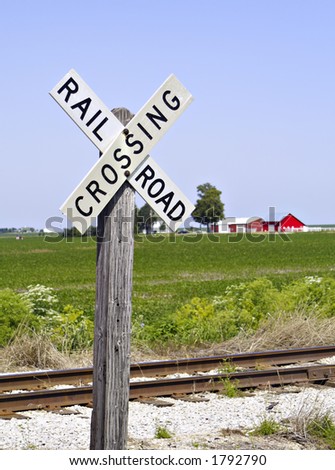 An old-fashioned railroad crossing sign with a farm scene in the background