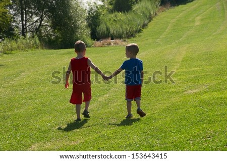Two brothers holding hands walking along the hill toward the beach on a hot summer day