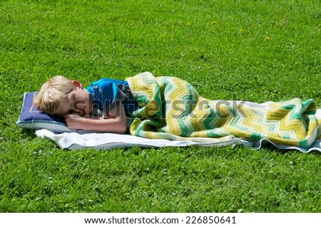 Anytime is the right time for a nap so the little boy lays down on the grass and covers himself with a blanket