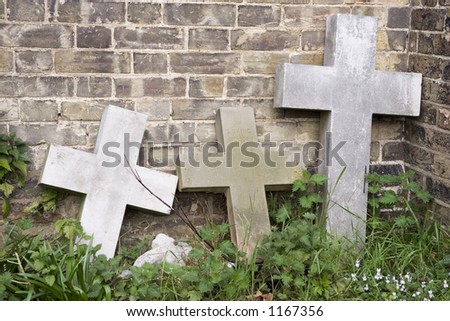 Three stone cross head stones against wall.