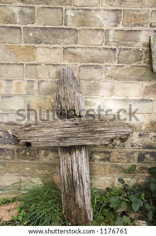 A rotten cross head stone against wall.