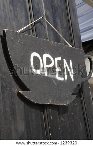 A open door sign in the shape of a tea cup on a wooden door..