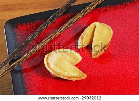 Two fortune cookies on a red plate with chop sticks