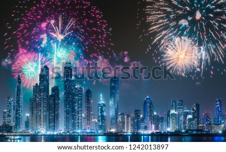 Modern buildings on Dubai Marina bay at night with fireworks and reflection on water, UAE.