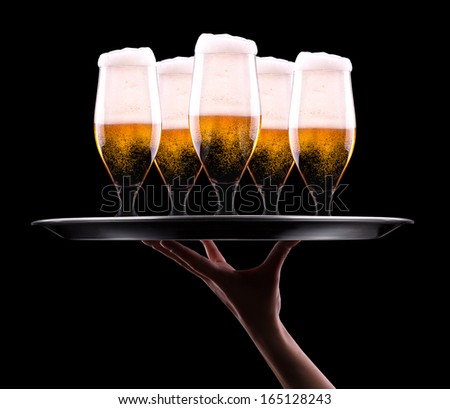 waiter hand and tray with Beer into glass on a black
