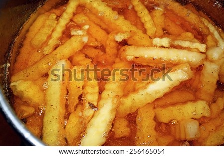 Crinkle Cut french fries sitting in a pot of oil in deep fryer