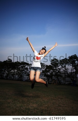 a beautiful cheerfully asian young girl jumping in the field with smiley face and blue sky.