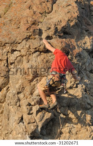 A Young Mountain Climber Jumps For A Rock Step On A Steep Mountain Side
