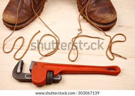 Pair of work boots with red adjustable wrench on wooden background. There written the word \'work\' by laces.