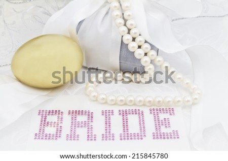 Feminine image of wedding day financial savings start.  Gold nest egg placed with BRIDE in pink letters surrounded by white ribbon, gray velvet gift box, and pearl necklace.
