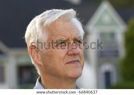 Close up portrait focus on senior man with unfocused house outlines behind him reflect the universal effect of difficult economic housing conditions