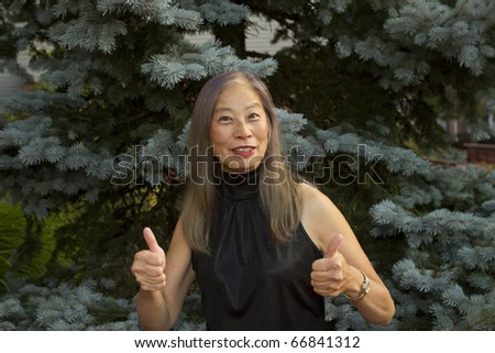 Senior Asian woman gives the thumbs up sign of success and approval