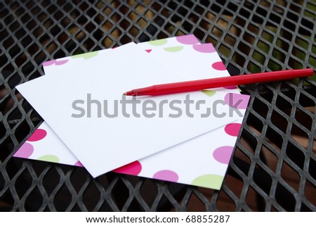 Red pen and note paper placed on black wrought iron patio table top with deck fencing barely visible