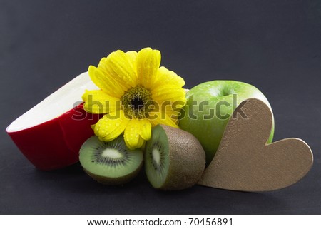 Heart healthy fruit and calcium rich cheese are fresh diet staples shown on a black background with gold heart in front and fresh blood with water drops neat to green apple and kiwi