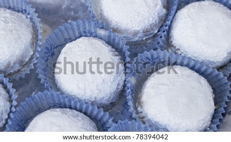 Kourambiethes, a Greek shortbread cookie, is covered with confectioner\'s sugar, and the finished cookie is nestled in blue paper.