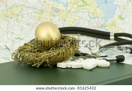 Gold egg sits in gold nest on lab book with pills and stethoscope in front of a map background.  Selective focus on gold nest egg and pills.