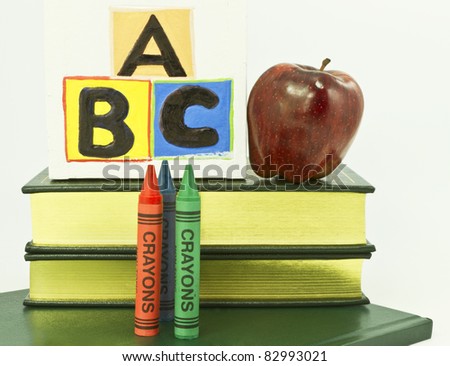 Three crayons, ABC blocks, red apple placed on books on white background