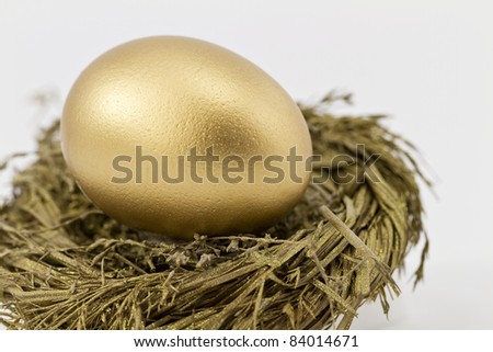 Closeup of gold nest egg set in sparkling gold nest; selective focus on nest egg;