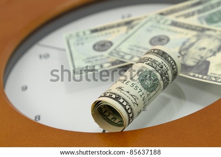 American currency placed on face of clock is indicative of time\'s relationship to money in investments, unique financial times, and financial urgency at specific points in life.