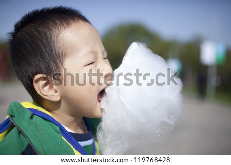 asian boy eating cotton candy happily in the park