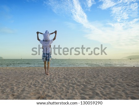 Father holding son on his shoulders at the beach with blue sky