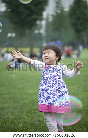 Cute asian little girl plays with a giant bubble outside in the park
