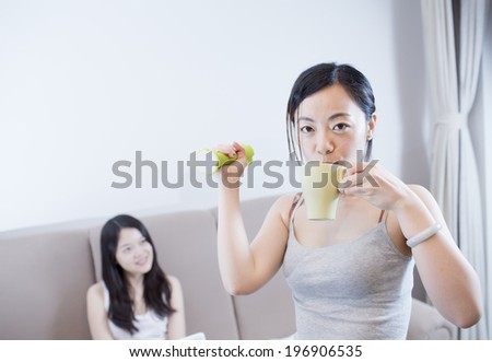 Young happy woman exercising with dumbbells at home with her friend