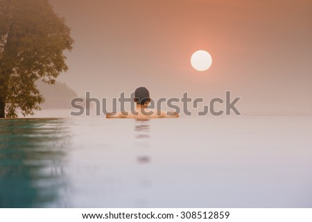 Silhouette of asian person  at the edge of infinity swimming pool,looking at the Ocean sunset