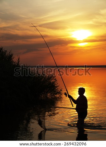 Fisherman catches fish by spinning on the lake at sunset