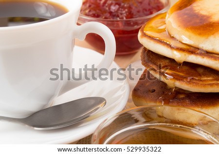 Pancakes with honey, strawberry jam and a cup of coffee close-up with shallow depth of focus