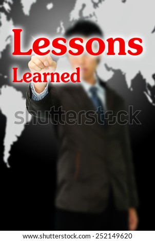 Business man pointing to transparent board with text: Lessons Learned
