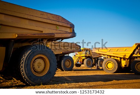 Four large yellow trucks used in modern mines and quarries for hauling industrial quantities of ore or coal. Photographed at sunset in golden light. Blackwater, Australia. Logos removed in Photoshop.