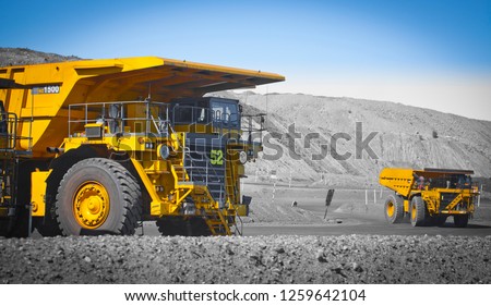 Spot color trucks, two large yellow truck used in a modern coal mine in Queensland, Australia. Trucks transports coal from open cast mine. Fossil fuel industry, Environmental challenge. Logos removed.