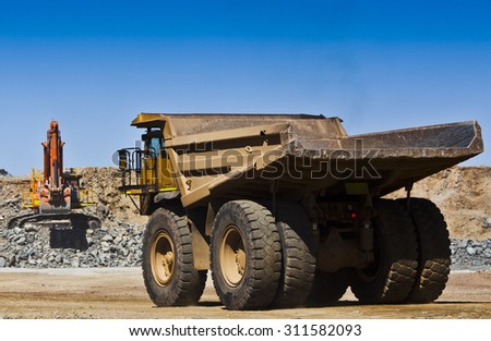Mining scene. Large truck drives towards digger to fill with ore from open cast mine. All logos removed.