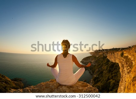 Young beautiful yoga woman meditating in lotus pose on the precipice of a cliff overlooking the sea. Yoga girl on the top of mountain on background of blue sea Crimea.