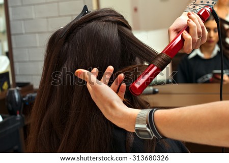 Fashion hairdresser doing hairstyle to young woman client making perm professional styler for curl on the background of a professional hairdressing salon.