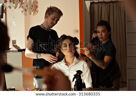 Backstage prepare young beautiful modeling stylist hairdresser and makeup artist working on models in the way of professional beauty salon. Work up artist and hairdresser at the salon- stock photo.