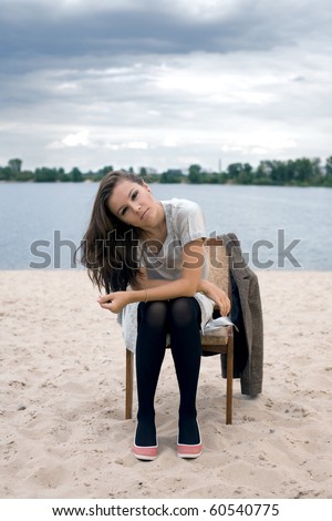 A charming young girl sits on a chair on the beach