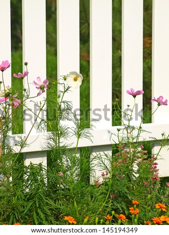 White fence on green grass with flowers taken closeup.