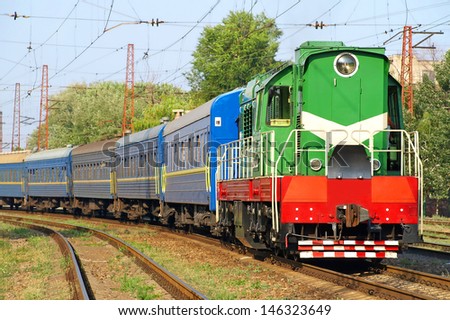 Green locomotive and blue passenger cars on the rails.