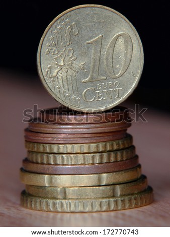 Ten euro cent coin balancing on a top of coins pile taken closeup.