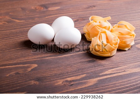 pasta raw three circles and three white eggs on a brown wooden table top view