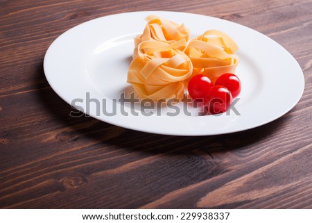pasta raw three circles and three cherry tomatoes on a white plate on brown wooden table top view