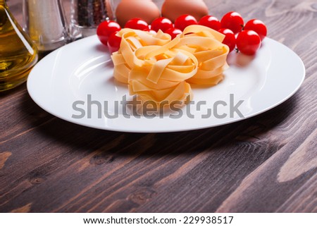 pasta raw three slices and a sprig of cherry tomatoes on a white plate on brown wooden table top view