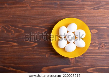 white eggs in yellow plate on brown table top view on the left space for text