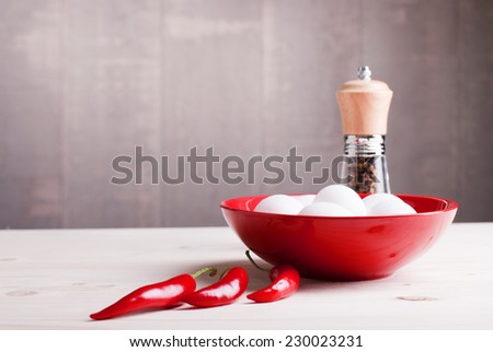 white eggs in a plate of red chili pepper on a light wooden table on the left side view of a place for text