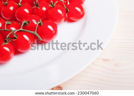 branch of cherry tomatoes in a white plate on a light wooden table top view and side view