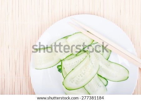 Japanese cucumber salad with thinly sliced cucumbers, close-up in white plate with Japanese shelves, rests on  bright straw view from above