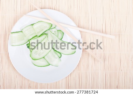 Japanese cucumber salad with thinly sliced cucumbers in white plate Japanese shelves, rests on  bright straw view from above