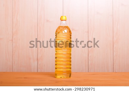Bottle of sunflower oil is on the yellow table in the center, on  background of light fence, side view